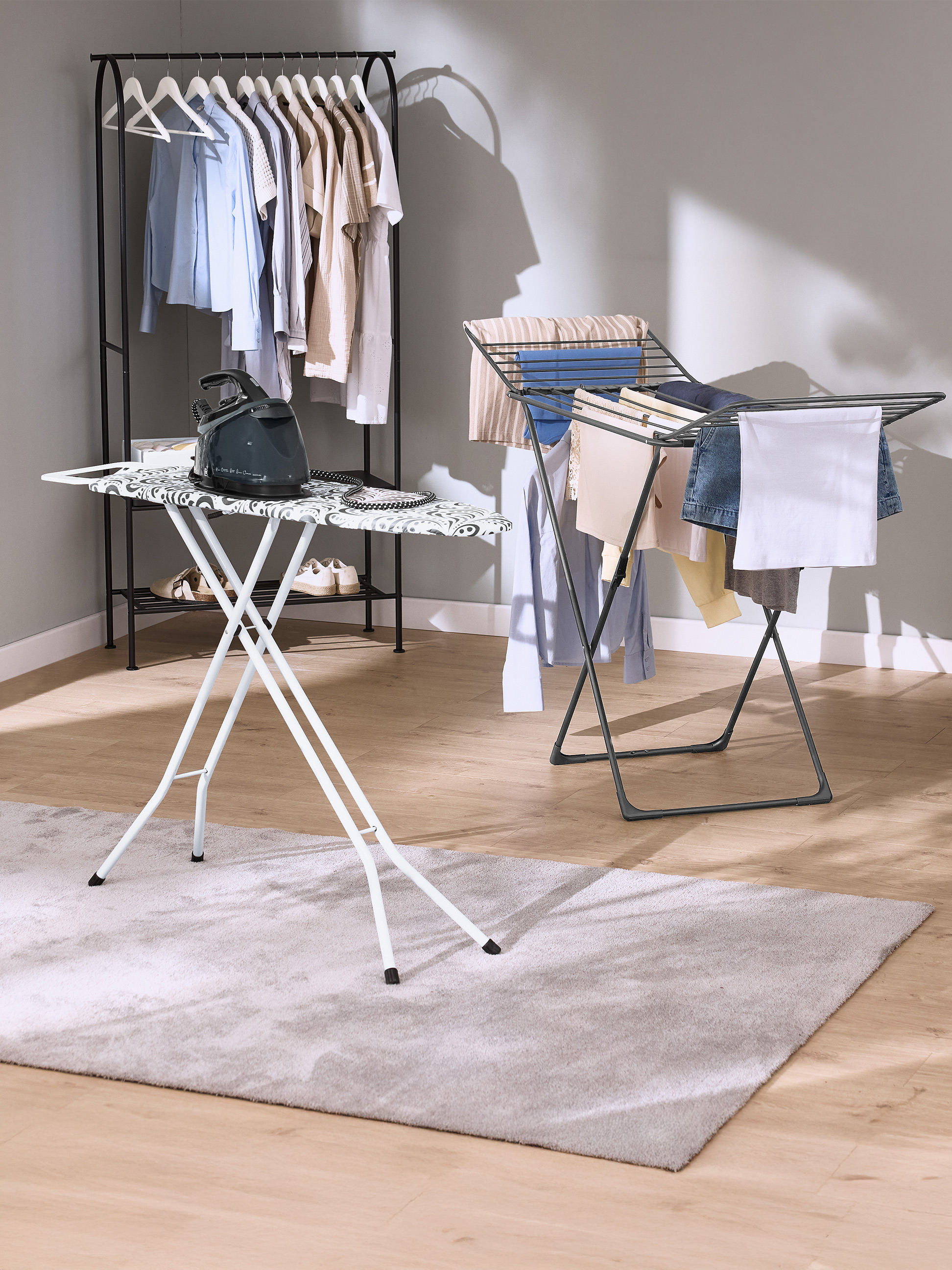Table à repasser avec fer et étendoir à linge avec vêtements dans une pièce.