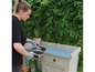 Een vrouw gebruikt een borstel om aarde van een houten werktafel met een metalen blad te vegen.