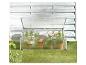 Aluminium en polycarbonaat kas met potplanten op groen gras tegen een witte muur.