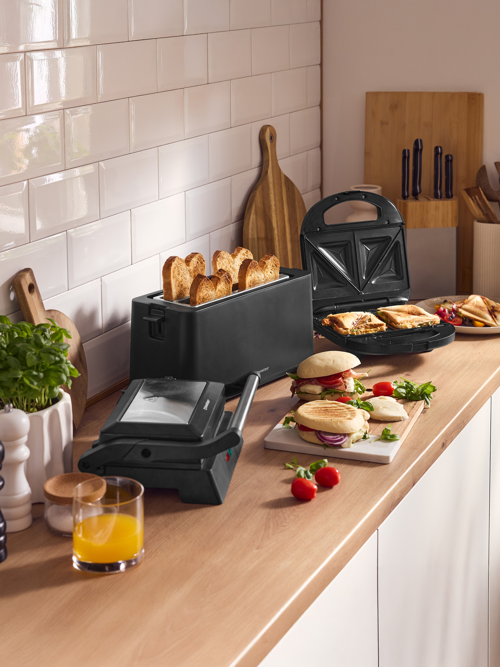 Aanrecht met broodrooster, tosti-ijzer en grillpers, bereide broodjes en sap.