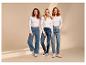 Trois femmes en hauts blancs à manches longues et jeans, souriant à la caméra.