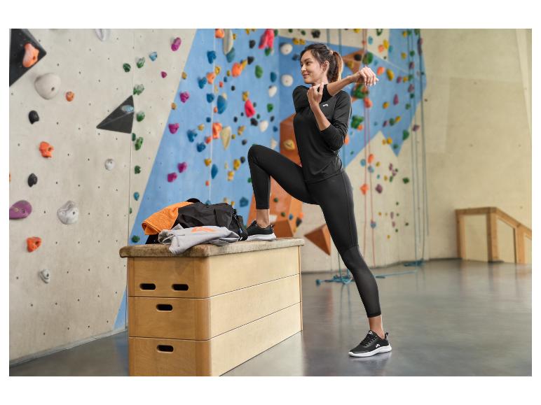 Femme en tenue de sport noire s'étirant près d'un mur d'escalade avec équipement.