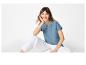 Femme en t-shirt bleu brodé et pantalon blanc, assise.