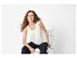 Femme en débardeur blanc et pantalon foncé assise sur une chaise, souriante et regardant de côté.