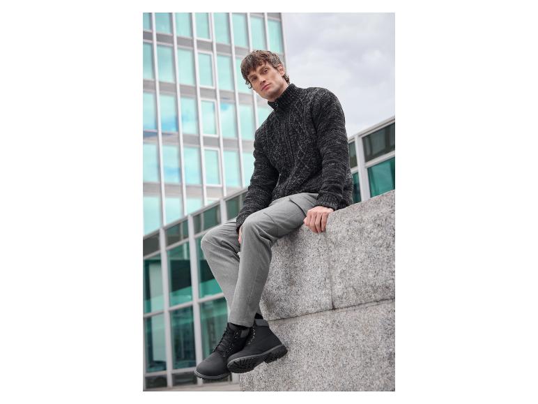 Un homme porte un pull noir et un pantalon gris avec des bottes Timberland noires.