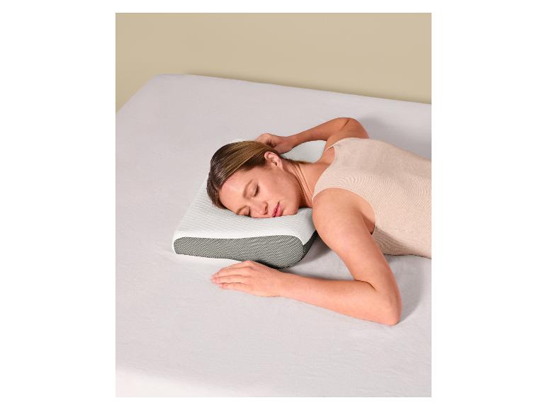 Vrouw slaapt op een wit en grijs ergonomisch kussen op een bed met witte lakens.