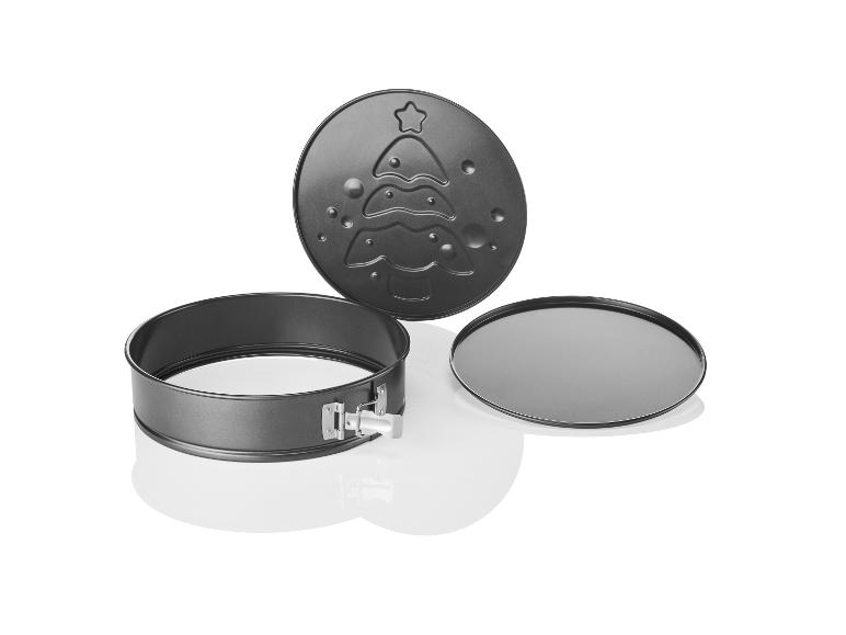 Un moule à pâtisserie rond avec un fond amovible, un couvercle à motif d'arbre de Noël et une plaque de cuisson supplémentaire.