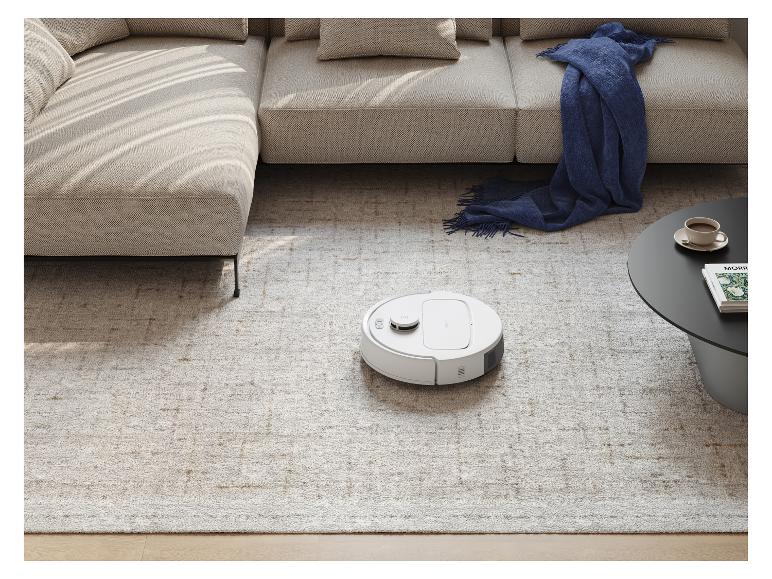 Robotstofzuiger op een licht tapijt in een moderne woonkamer met een bank en salontafel.