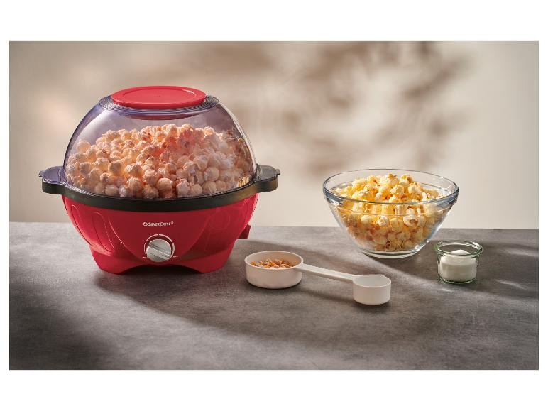 Machine à popcorn rouge pleine de popcorn, avec un bol de popcorn et des ingrédients sur une table.