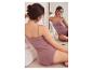 Vrouw in een mauve hemdje en slipje kijkt naar haar spiegelbeeld.