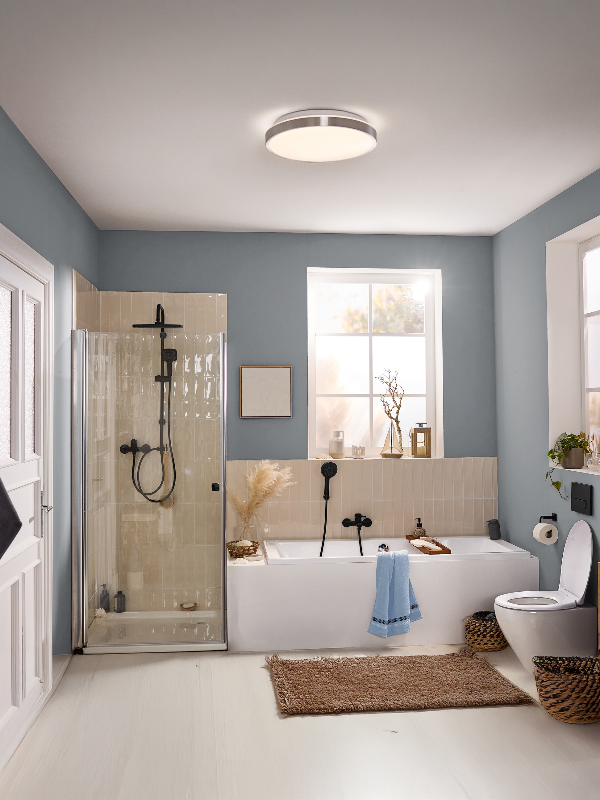 Salle de bain moderne avec murs bleus, cabine de douche, baignoire, toilettes et plafonnier rond.