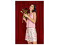 Une femme portant un top rose et une jupe à fleurs tient une fleur rouge.