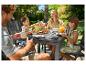 Famille prenant le petit-déjeuner en plein air à une table de jardin avec nourriture et boissons.