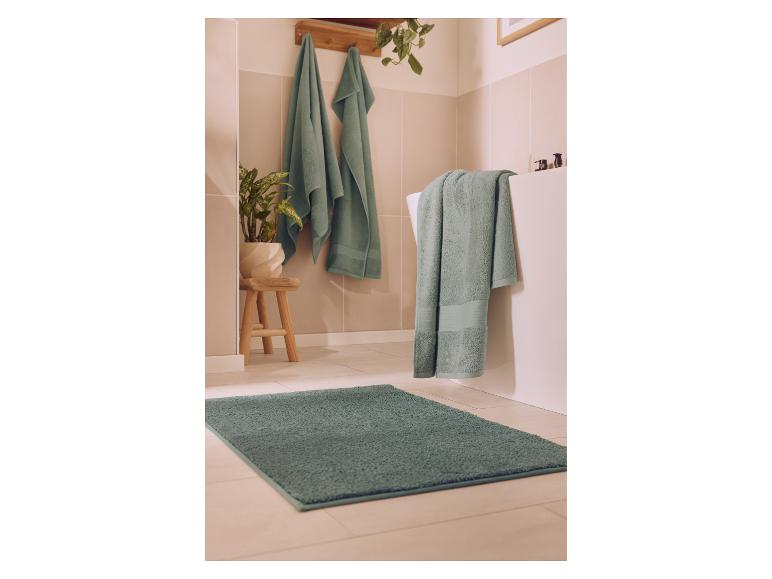 Badkamer met groene handdoeken en vloerkleed, een plant en een houten krukje.