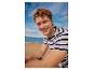 Man in gestreept T-shirt lachend op het strand.
