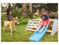Deux enfants jouent dehors avec un cheval à bascule en bois et une structure de jeu en bois avec toboggan.