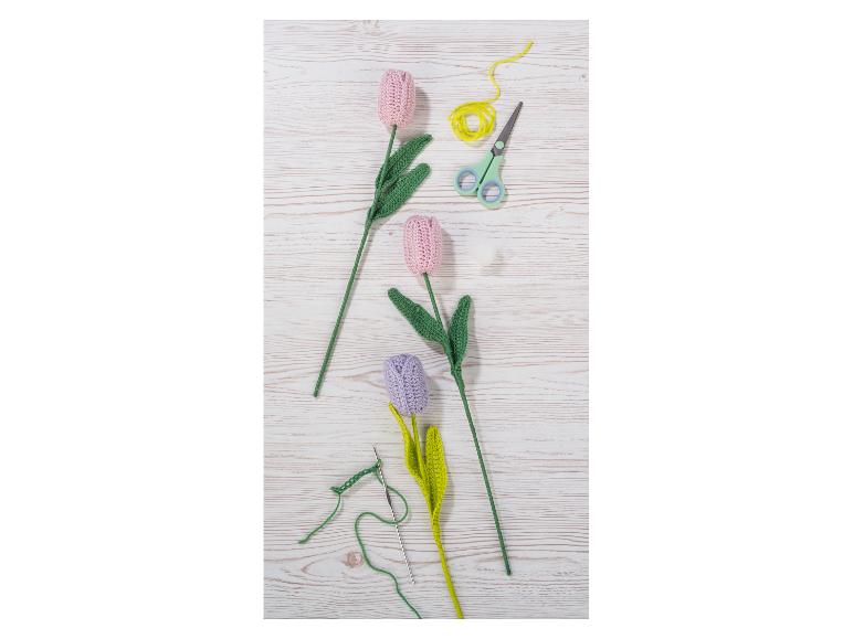 Tulipes au crochet roses et violettes avec du fil, des ciseaux et un crochet sur une table en bois.