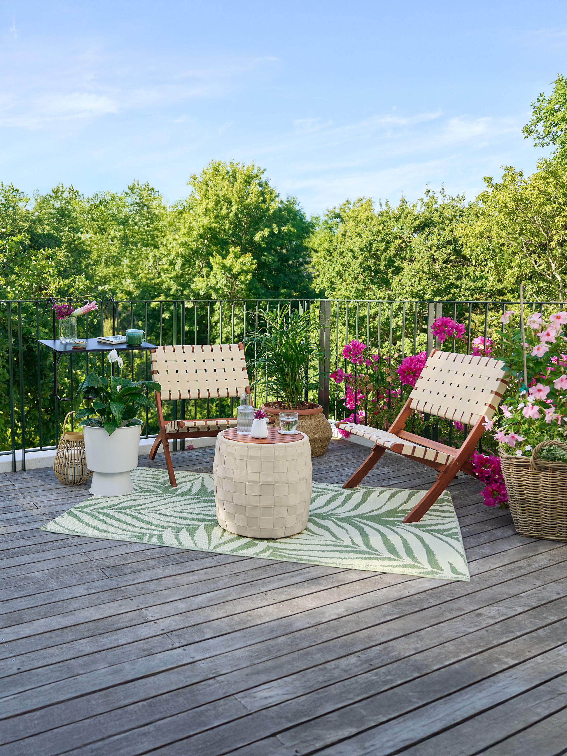 Balcon avec deux chaises, une table, un tapis et des fleurs.