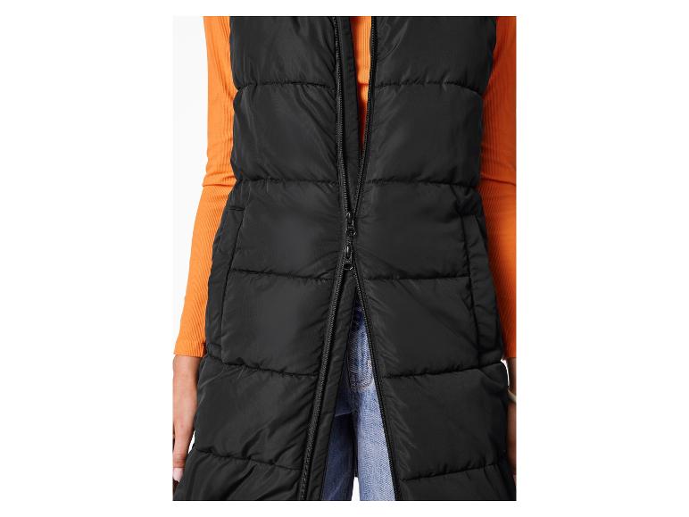 Zwart lang gewatteerd vest met een oranje shirt met lange mouwen en jeans.