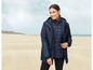 Une femme porte un parka bleu marine avec une veste intérieure matelassée sur une plage.