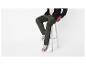 Un homme porte un pantalon cargo vert, une chemise noire et des baskets marron, assis sur un tabouret.