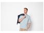 Homme souriant en t-shirt bleu clair et pantalon beige, tenant une veste foncée.