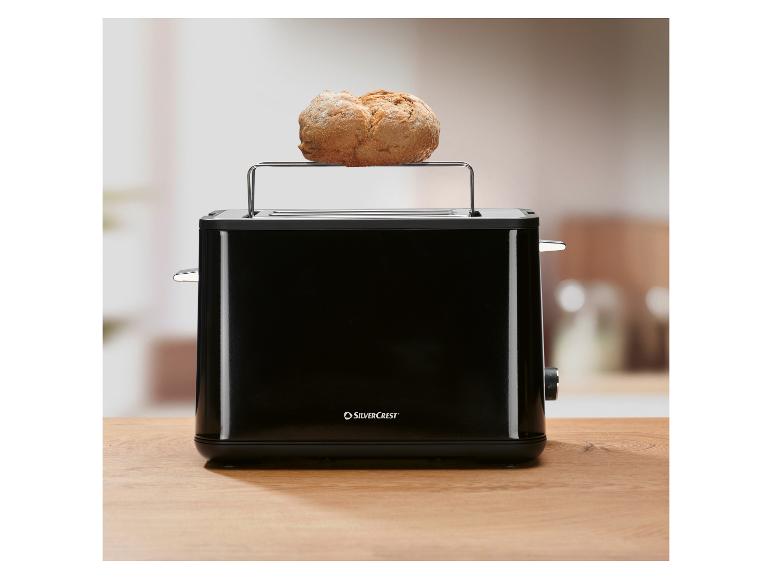 Zwarte broodrooster met een rond broodje op het opwarmrek, op een houten tafel.