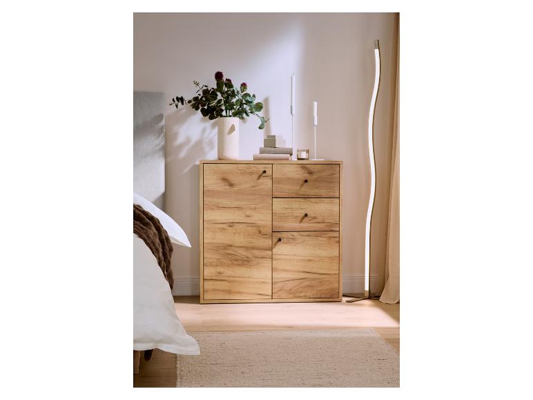 Houten ladekast met lades en deuren, versierd met een vaas bloemen en kaarsen, naast een bed.