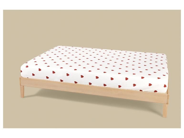 Wit hoeslaken met rode hartjes op een licht houten bedframe.