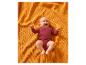 Een lachende baby in een rode romper ligt op een oranje getextureerde deken.