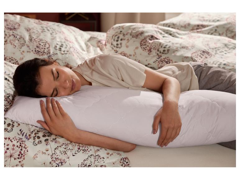 Une femme dort dans son lit en serrant dans ses bras un oreiller de corps blanc LIVARNO home.