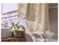 Beige handdoeken met een patroonrand hangen in een badkamer met plant en wastafel.