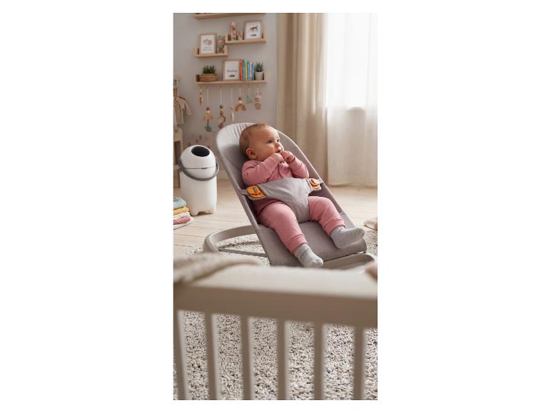 Bébé dans un transat en tissu gris dans une chambre d'enfant avec étagères en bois et décor.