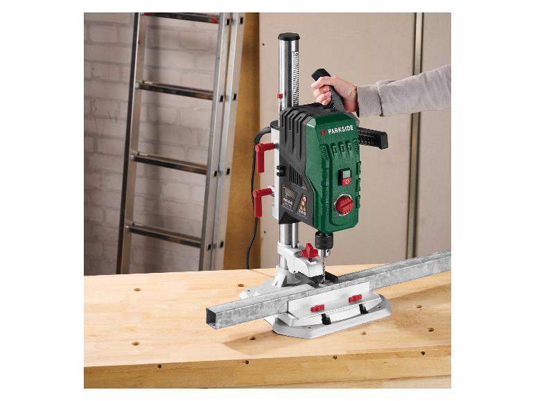 Een persoon gebruikt een Parkside kolomboormachine om een metalen staaf op een werkbank te boren.