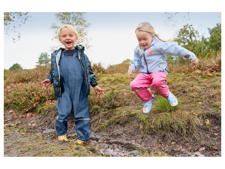 Deux enfants heureux en vestes et salopettes imperméables jouant dans des flaques de boue.