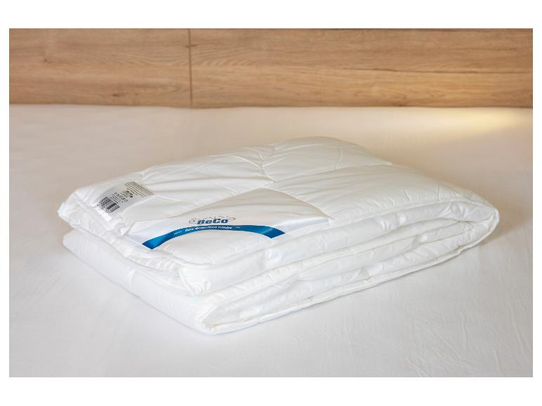 Couette blanche BeCo pliée sur un lit avec une tête de lit en bois.