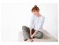 Femme en t-shirt blanc à manches longues et pantalon à carreaux assise sur un pouf beige.