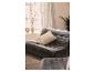 Grijze fluwelen bank met beige kussen en plaid, naast een raam met decoratieve vazen.