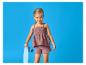 Lachend meisje in een mauve top- en shortset, met een lichtblauw skateboard.