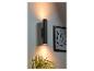 Un luminaire mural noir cylindrique éclaire une pièce avec une plante et un tableau.