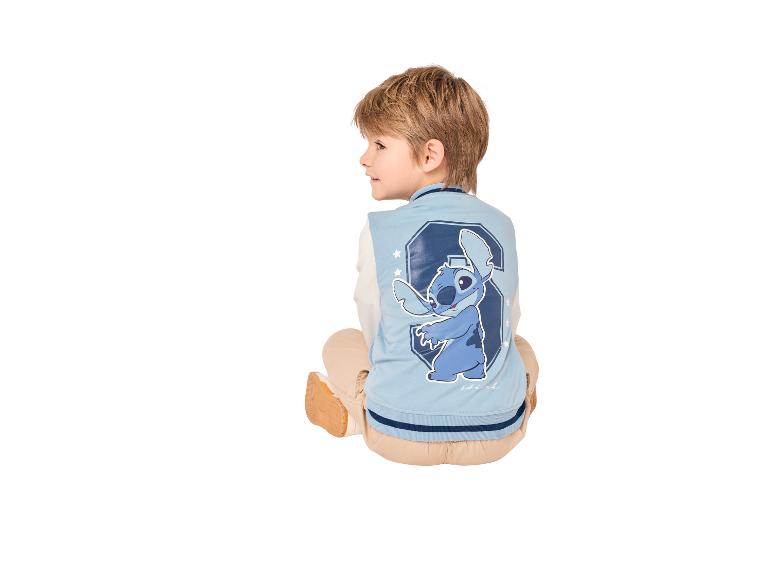 Jongen in een lichtblauwe varsity-jas met een cartoonfiguurprint op de rug, zittend.