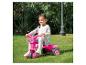 Een meisje rijdt op een roze Barbie driewieler in de tuin.