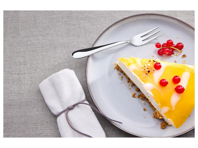 Een stuk cheesecake met mangotopping en rode bessen op een bord met een vork.
