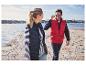 Een man en vrouw in blauwe en rode bodywarmers lopen langs de kust.