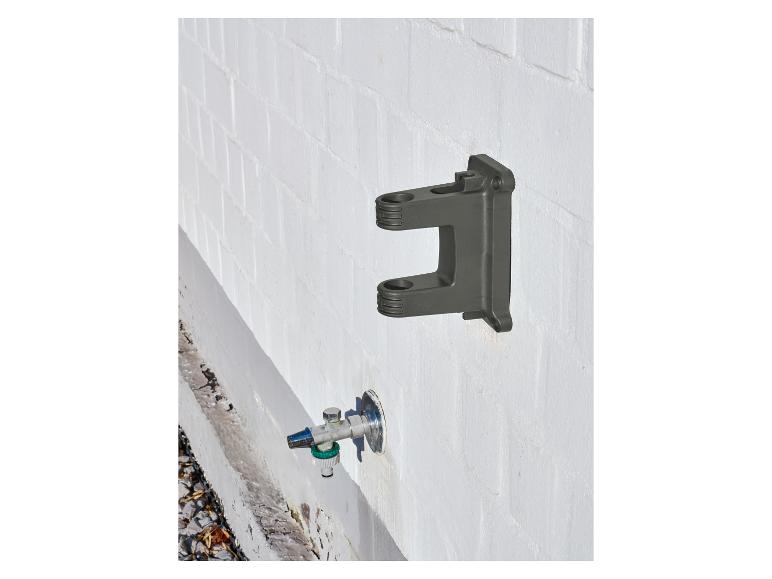 Support mural gris foncé et robinet d'eau avec raccord de tuyau sur un mur de briques blanc.