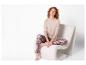 Femme aux cheveux roux bouclés en haut beige à manches longues et pantalon de pyjama à carreaux sur une chaise blanche