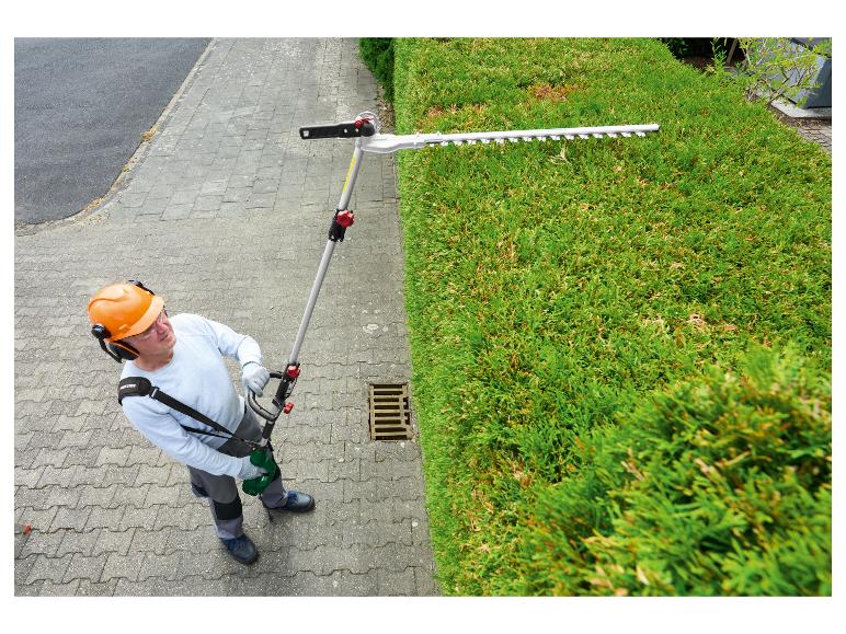 Man snoeit een heg met een lange heggenschaar, met veiligheidsuitrusting.
