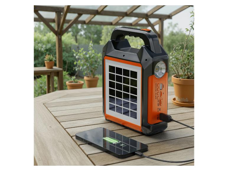 Chargeur solaire portable noir et orange avec un téléphone en charge sur une table en bois.