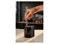 Une main insérant un crayon en bois dans un taille-crayon électrique noir sur une table en bois.