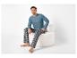 Man in blauw shirt met lange mouwen en geruite pyjamabroek zittend in een witte fauteuil.